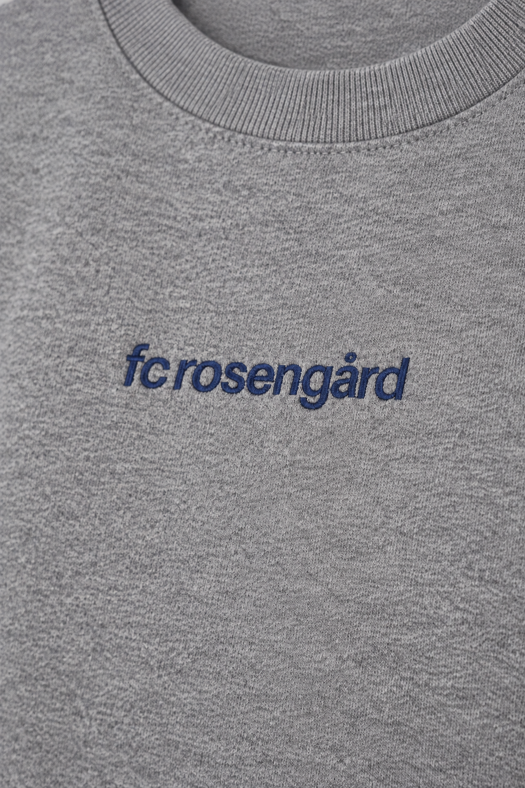 Studio-lit detail shot of the navy fcrosengård embroidery on the grey crewneck