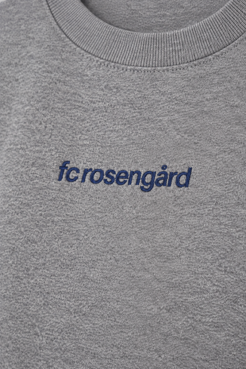 Studio-lit detail shot of the navy fcrosengård embroidery on the grey crewneck